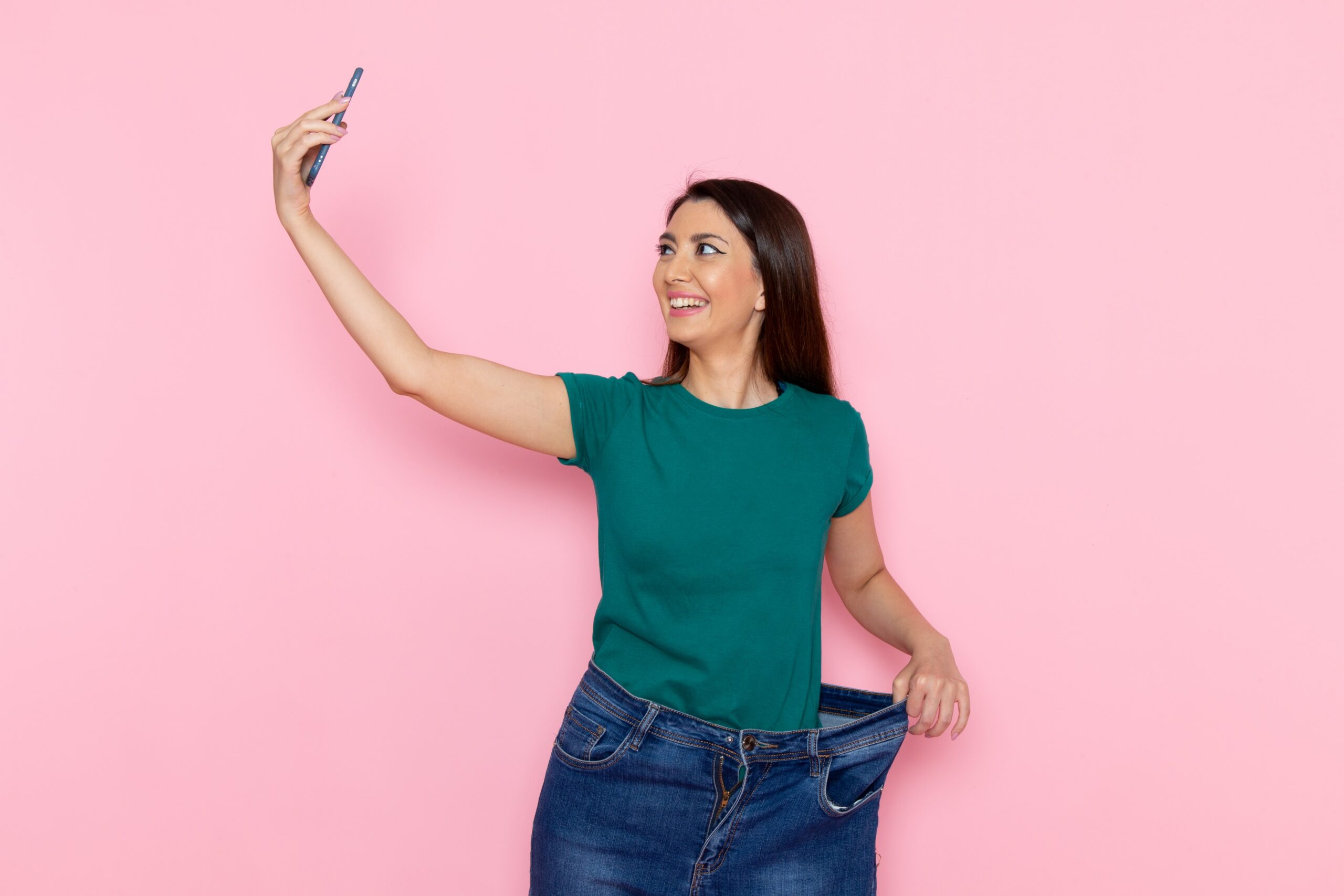 Mulher sorrindo enquanto faz uma selfie, mostrando como sua calça ficou folgada após perda de peso com Ozempic.